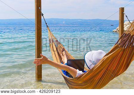 Work From Anywhere. Young Smilyng Woman, Female Freelancer In Straw Hat Working On Laptop On Beach.