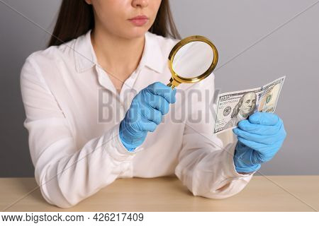 Expert Authenticating 100 Dollar Banknote With Magnifying Glass At Table On Light Grey Background, C