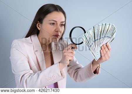 Expert Authenticating 100 Dollar Banknotes With Magnifying Glass On Light Grey Background. Fake Mone