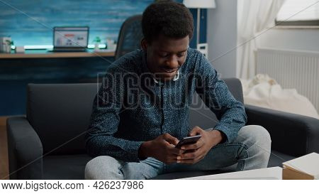 Black Guy In His Living Room Using Phone To Browse Social Media, Internet Connection And Communicati