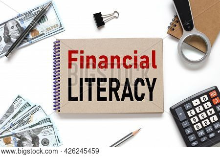 Financial Literacy. Notebook On White Workspace. Near The Notepad Dollar Bills And A Calculator
