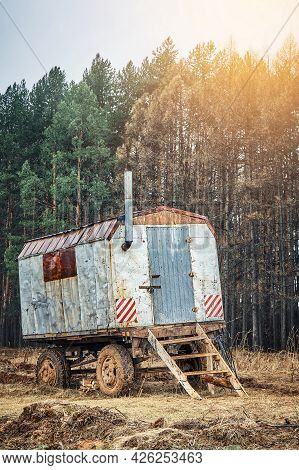 Old Rusty Metal Semi Trailer House With Chimney And Wooden Steps Stands On Field By High Pine Trees 