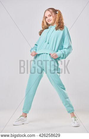 Carefree cute teenage girl in trendy mint hoodie and sweatpants poses on a white background. Positive emotions. Youth style. Full length portrait. 