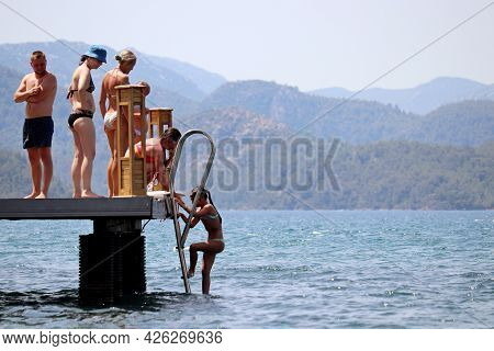Hisaronu, Turkey​ -​ July 2021: People With Children Having Fun On A Beach On Green Mountains Backgr
