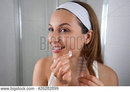 Beautiful Smiling Girl Applying Acne Treatment Patch On A Pimple In Bathroom