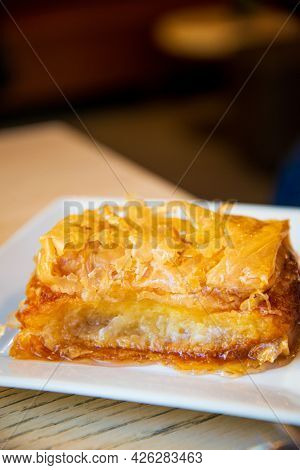 Delicious Greek sweet pastry named Galaktoboureko, made of semolina custard in filo, served with honey in white plate.