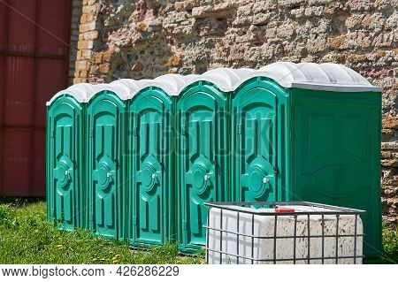 Group Of Green Plastic Bio Toilet Cubicles Against A Background Of Stone Wall