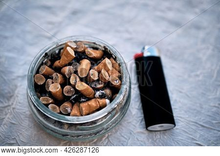 Ashtray Filled Up With Cigarette Ends And Black Lighter