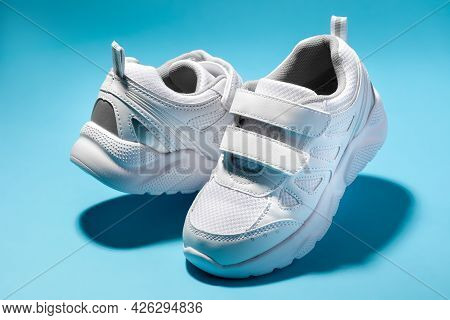 Macro Of Two White Childrens Floating Sneakers With Velcro Facing Each Other Isolated On A Blue Back
