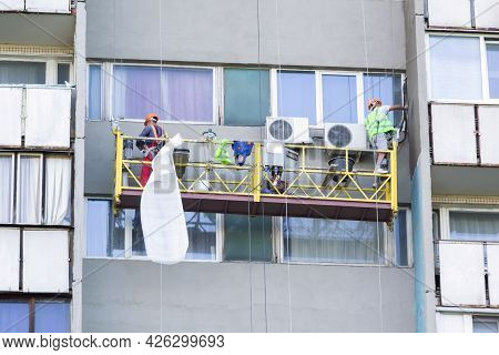 Workers On The Lift Paint The Exterior Wall Of A Residential Building