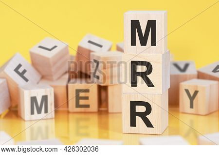 Wooden Cubes With Letters Mrr Arranged In A Vertical Pyramid, Yellow Background, Reflection From The