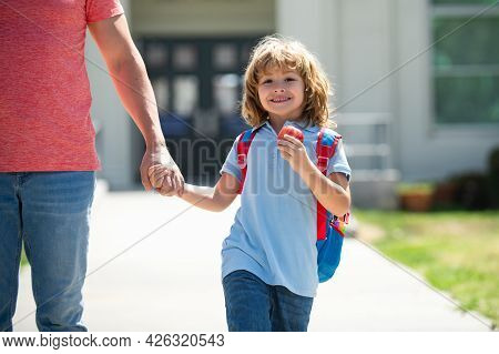 American Father And Son Walking Trough School Park. First Day At School. Father Leads A Little Child
