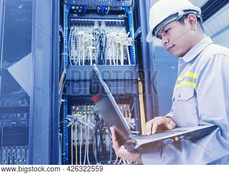 A Man With A Laptop Sits In The Server Room Of The Data Center. The System Administrator Works Near 