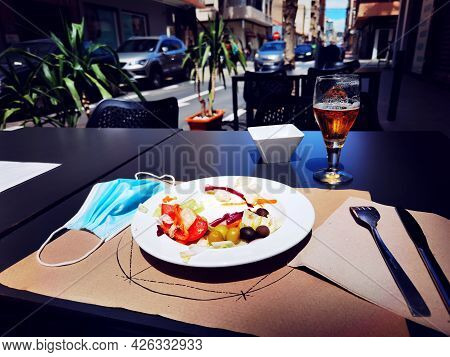 Medical Mask On The Serviced Table. Work Of The Cafes And Restaurants During Covid-19 Pandemic