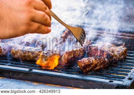 Preparing Meat Rolls Called Mici Or Mititei On Barbecue. Close Up Of Grill With Burning Fire With Fl
