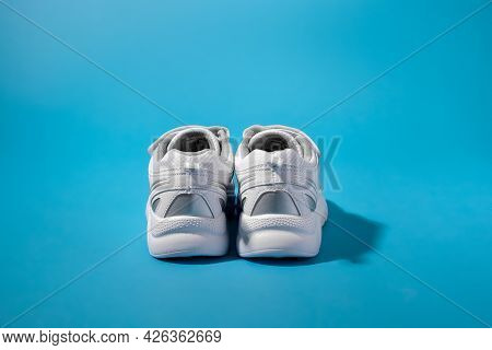 Rear View Of Two Backs Or Heels Of White Sneakers For Children With Silver Inserts On A Blue Paper B