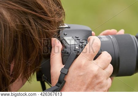 A Cut-off Image Of A Woman With A Camera. She Looks Into The Viewfinder, And Her Hand Presses The Sh