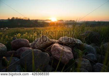 Sunrise Landscape With Roks On The Siede Of The Meadow And Field. Summertime Scenery Of Northern Eur