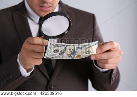 Expert Authenticating 100 Dollar Banknote With Magnifying Glass On Light Grey Background, Closeup. F