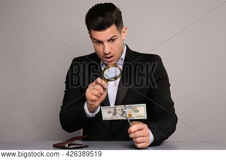 Expert Authenticating 100 Dollar Banknote With Magnifying Glass At Table On Light Grey Background. F