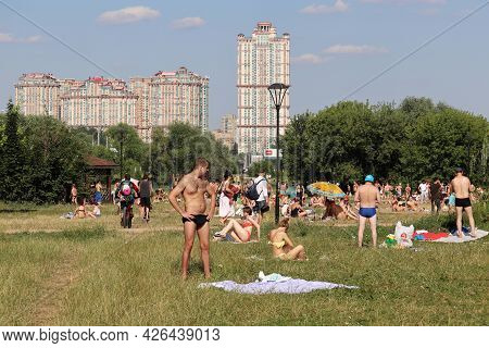Moscow, Russia - July 2021: Crowd Of People Sunbathing On A Green Lawn On Background Of Residential 