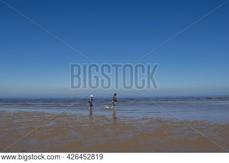 Old Hunstanton, Norfolk, England - June 13 2021. Couple On The Beach With Their Dog During Low Tide 