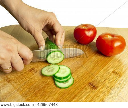 The Hands Of An Unrecognizable Woman Cut A Cucumber On A White Background.