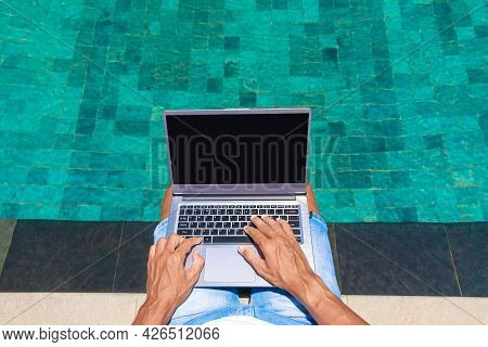 A Man Works On A Laptop By The Pool. Freelance, Work In Nature. Hands Are Typing Text.