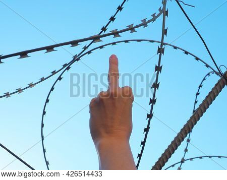 Hand Showing Middle Finger On Background Of Barbed Wire And Blue Sky