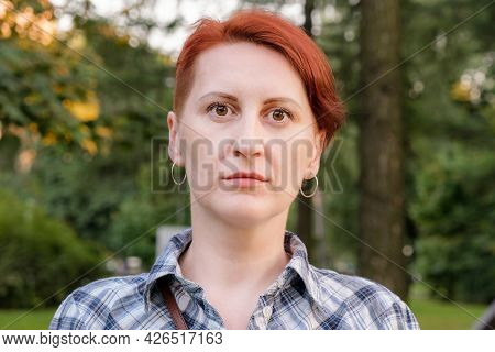 Simple Portrait Of A Red-haired Young Woman With Short Hair. Woman In A Checkered Shirt Against The 