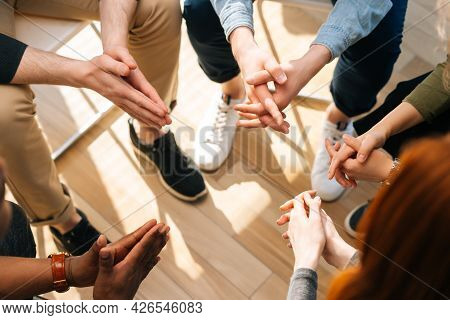Close-up Top View Of Group Diverse Multiethnic People Sitting In Circle With Hands Crossed Hands Tog