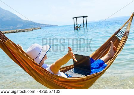 Work From Anywhere. Young Smilyng Woman, Female Freelancer In Straw Hat Working On Laptop On Beach.