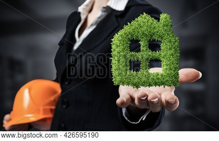 Real Estate Agent Holds In Palm Green Plant In Shape Of House. Woman In Business Suit With Safety He