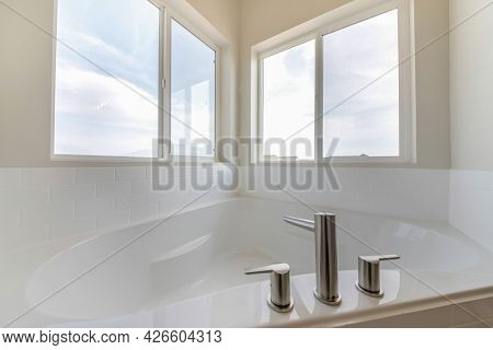 Corner Bathtub In A Bathroom With Widespread Faucet Against The Windows