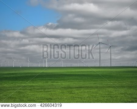 Eolian Farm Renewable Energy In Fresh Green Field Against Clear Blue Sky