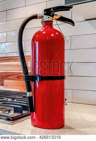 Vertical Fire Extinguisher And Cooktop With Kettle On The Countertop Inside Home Kitchen