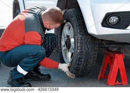 A Car Mechanic In A Medical Mask Changes A Wheel On A Car On The Street On A Sunny Day. Help On The 