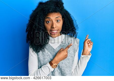 African american woman with afro hair wearing casual winter sweater pointing aside worried and nervous with both hands, concerned and surprised expression 