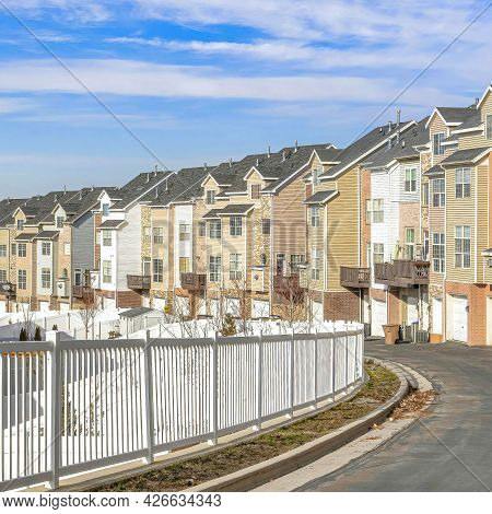 Square Townhouses Along Road With White Fence Against Scenic Blue Sky And White Clouds