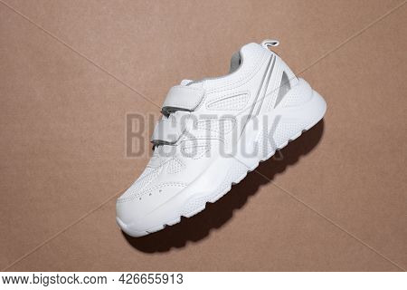 Flat Lay One White Kid Sneakers With Velcro Fasteners On The Side With Hard Shadows In The Center Is