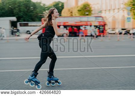 Outdoor Shot Of Active Slim Young Woman Enjoys Rollerskating During Spare Time Dressed In Blackactiv