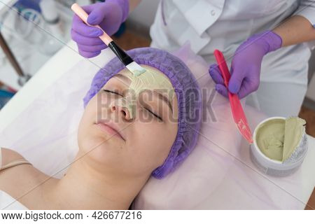 In The Beauty Salon, The Beautician Puts A Mask Of Green Clay On The Face Of A Young Girl. Daily Fac