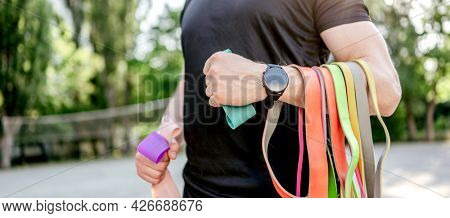 Strong man guy holding set of colorful elastic rubber bands at the stadium outdoors. Athlete male person during workout with additional sport equipmant