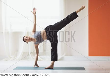 Young Woman Practicing Yoga, Performs The Ardha Chandrasana Exercise, The Crescent Moon Pose In The 
