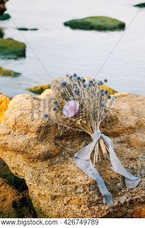 Vintage Wedding Bouquet Of Dried Flowers In Blue And Purple Shades On A Yellow Wild Stone By The Sea