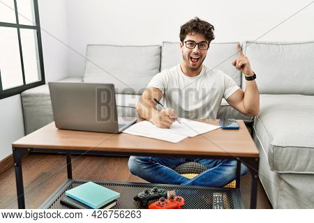 Hispanic man doing papers at home pointing finger up with successful idea. exited and happy. number one. 