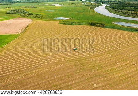 Aerial View Tractor Collects Dry Grass In Straw Bales In Wheat Field. Special Agricultural Equipment