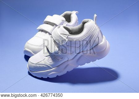 Macro Side View Two Flying White Kid Running Shoes With Velcro Isolated On Purple Background