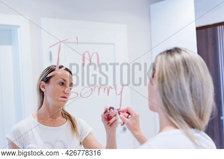 A Blonde With A Sad Face Writes The Words Im Sorry On The Mirror With Lipstick.