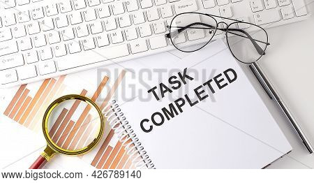 Task Completed Text Written On Notebook With Keyboard, Chart,and Glasses